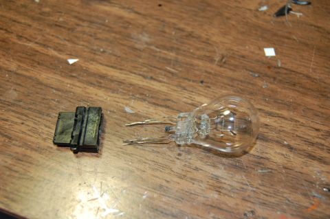 1985 Mercury Grand Marquis - A clear light bulb and its black socket sit on a wooden surface, with the Supermotors.net logo visible.