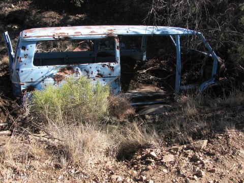 1996 Ford C-350 (Centurion Conversions) - Abandoned van body, heavily rusted and stripped, rests in a dry, brush-filled landscape.