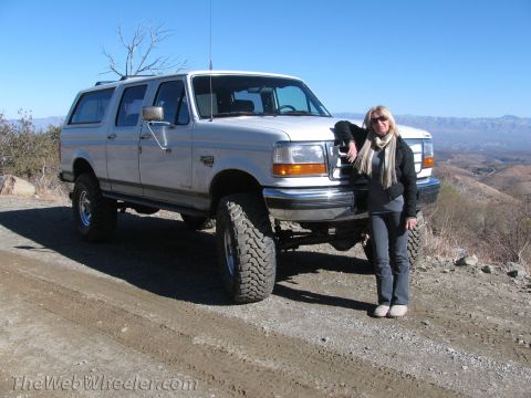 1996 Ford C-350 (Centurion Conversions) - Woman poses with a lifted 1996 Ford C-350 pickup truck on a dirt road with mountains in the background.