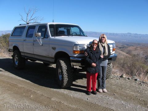 1996 Ford C-350 (Centurion Conversions) - Two women pose in front of a lifted Ford Bronco Centurion on a dirt road with a mountainous landscape in the background.