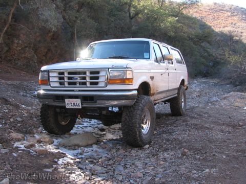 1996 Ford C-350 (Centurion Conversions) - This lifted SUV navigates a rocky, off-road path, its large tires gripping the uneven terrain.
