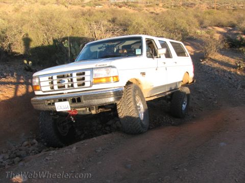 1996 Ford C-350 (Centurion Conversions) - A white Ford Bronco navigates a rocky off-road trail under a bright sun.