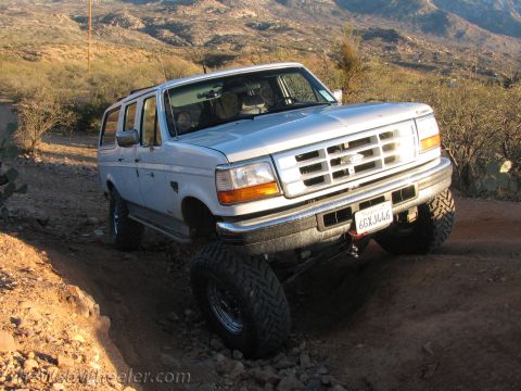 1996 Ford C-350 (Centurion Conversions) - A white Ford Bronco navigates a dirt trail with a mountainous desert landscape in the background.