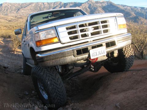 1996 Ford C-350 (Centurion Conversions) - A lifted 1996 Ford C-350 (Centurion Conversions) navigates a rocky off-road path with mountains in the background.
