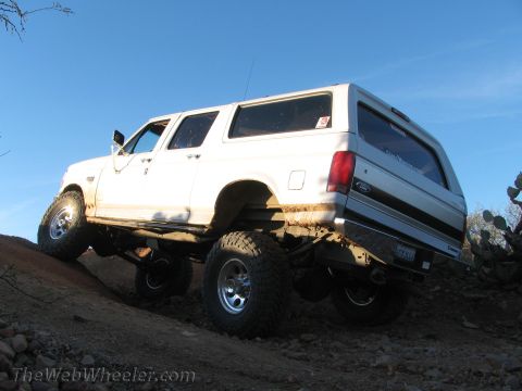 1996 Ford C-350 (Centurion Conversions) - White Ford Bronco SUV with lifted suspension and off-road tires climbing a dirt hill.