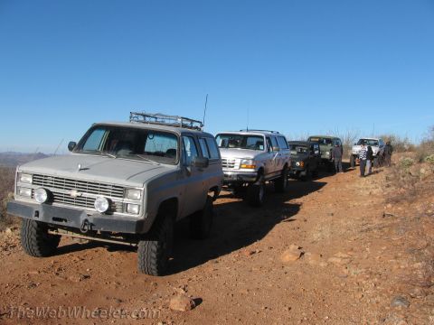 1996 Ford C-350 (Centurion Conversions) - A convoy of SUVs navigates a dusty, off-road trail under a clear blue sky.