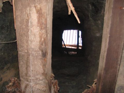 1996 Ford C-350 (Centurion Conversions) - A dark mine tunnel with rough wooden supports leads to a barred opening, suggesting an abandoned or secured location.