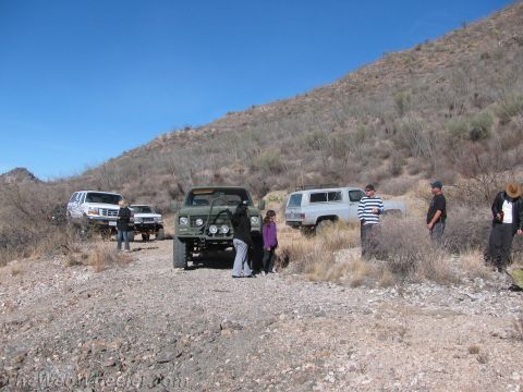 1996 Ford C-350 (Centurion Conversions) - A group of people and their off-road vehicles are gathered on a dusty trail under a clear blue sky.