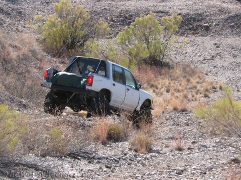 1996 Ford C-350 (Centurion Conversions) - A modified pickup truck navigates a challenging off-road terrain with sparse vegetation.