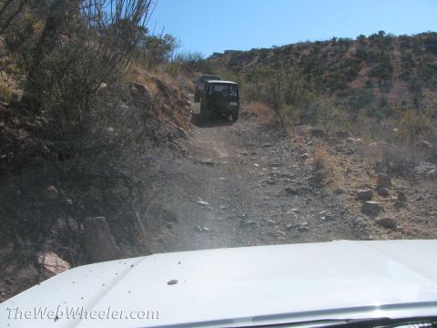 1996 Ford C-350 (Centurion Conversions) - Two SUVs navigate a rough dirt road in a desert environment under a clear blue sky.