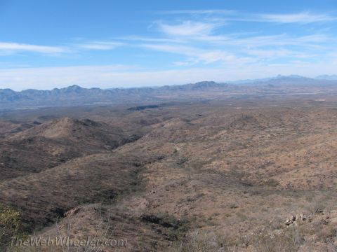 1996 Ford C-350 (Centurion Conversions) - A wide overlook across brushy desert ridges and canyons toward distant blue mountain ranges under a bright sky with thin cirrus clouds. No…