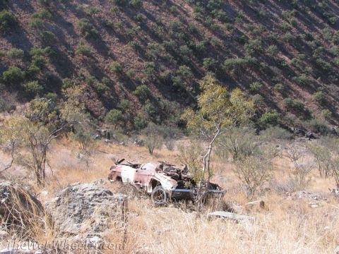 1996 Ford C-350 (Centurion Conversions) - A heavily damaged and rusted car sits in a dry, grassy field on a hillside.
