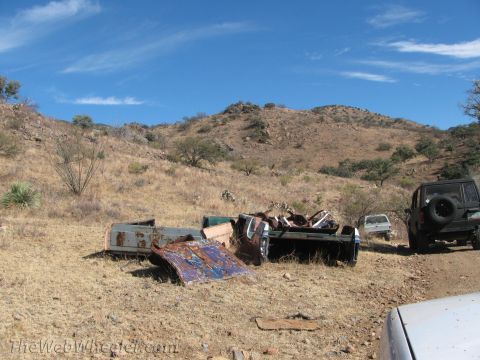 1996 Ford C-350 (Centurion Conversions) - Several old truck beds and parts are scattered in a dry, hilly landscape with a black SUV parked nearby.