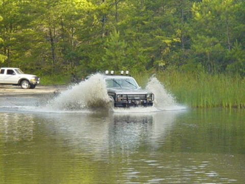 1980 Ford Bronco - Two trucks off-roading, one driving through a water obstacle.