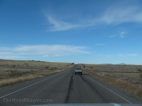 1996 Ford C-350 (Centurion Conversions) - A lone pickup truck travels down a long, straight highway in a vast, open, arid landscape.