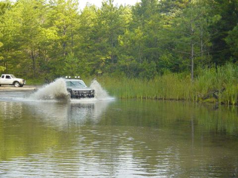 1980 Ford Bronco - An off-road vehicle navigates through a shallow body of water, creating a significant spray.