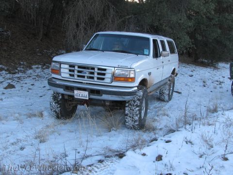 1996 Ford C-350 (Centurion Conversions) - A lifted white SUV sits in a snowy, wooded area, its large tires ready for off-road adventure.