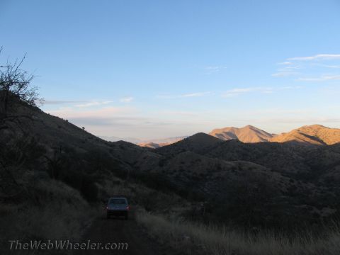 1996 Ford C-350 (Centurion Conversions) - A van travels a dusty mountain road as the sun sets, casting long shadows across the terrain.