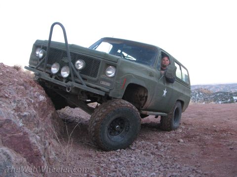 1996 Ford C-350 (Centurion Conversions) - A man drives an olive green SUV with a brush guard over rough, rocky terrain.