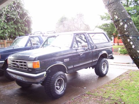 1988 Ford Bronco - 1988 Ford Bronco parked on a wet driveway next to another truck.