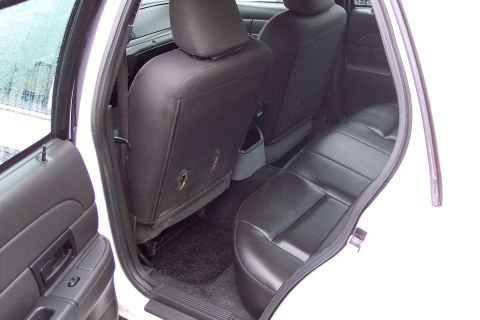 2001 Ford Crown Victoria - The interior of a white car reveals worn black leather rear seats and a dark carpeted floor.