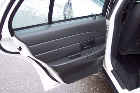 2001 Ford Crown Victoria - Interior view of a white car's door panel and rear seat, showing the black trim and door handle.