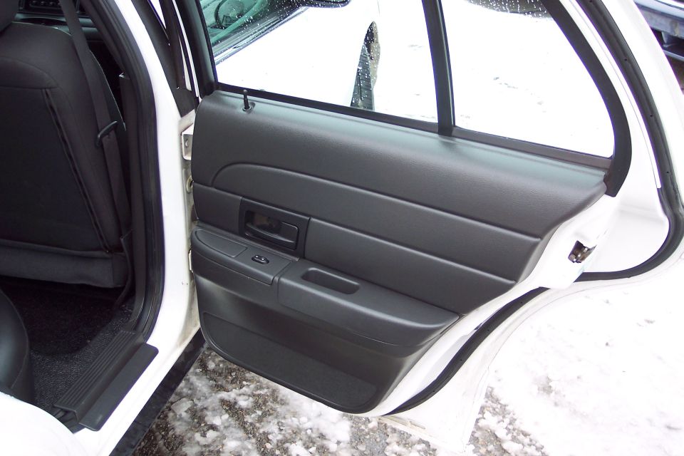 Interior shot of a white Ford Crown Victoria, showing the rear passenger door panel and part of the seat. Snow is visible on the ground outside