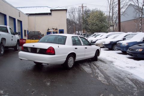 2001 Ford Crown Victoria - A white 2001 Ford Crown Victoria sedan is parked in a lot covered with snow, with other vehicles visible in the background.