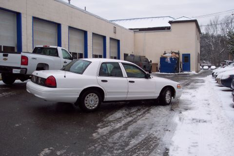2001 Ford Crown Victoria - White 2001 Ford Crown Victoria parked on a wet, snowy asphalt lot in front of a commercial building.