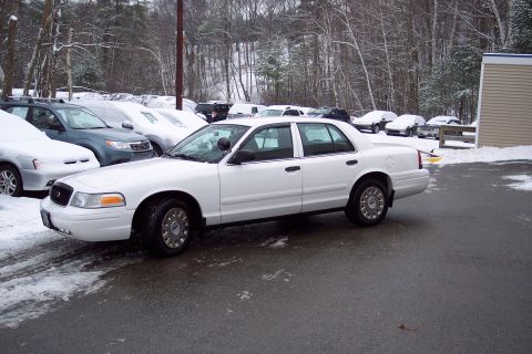 2001 Ford Crown Victoria - A white 2001 Ford Crown Victoria sedan is parked in a snowy lot, with other vehicles visible in the background.