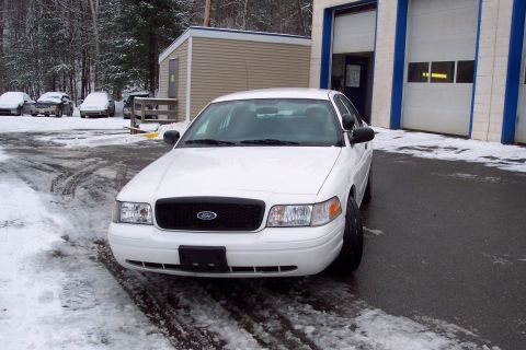 2001 Ford Crown Victoria - A white 2001 Ford Crown Victoria is parked in a snowy lot outside a garage.