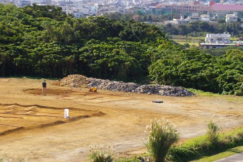 1986 Ford Bronco - A wide view of a construction site with a person and equipment, set against a backdrop of lush green trees and distant buildings.