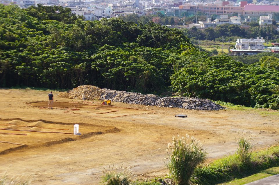 Construction site with dirt mounds, piles of rocks, a person, and a small yellow construction vehicle