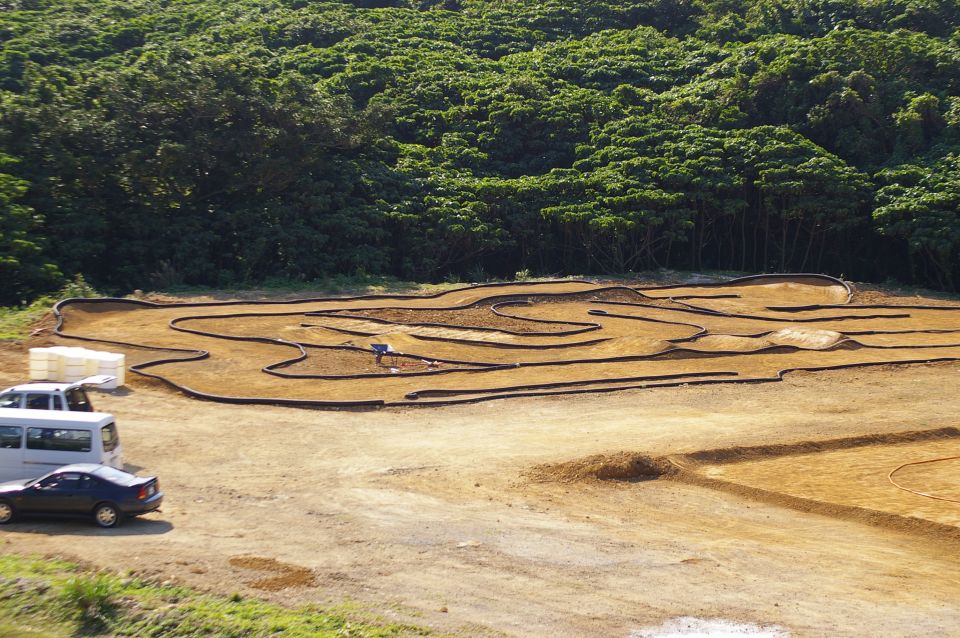 RC car track with a white van and a dark sedan parked on dirt