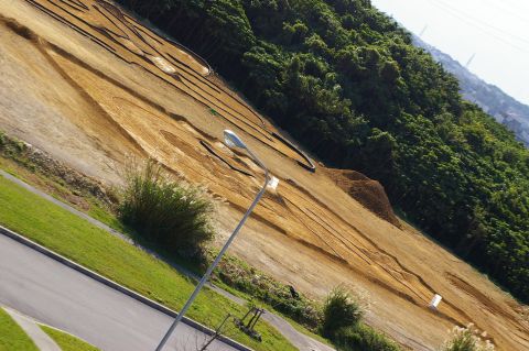 1986 Ford Bronco - RC car track on a dirt hillside with surrounding vegetation and a street in the foreground.