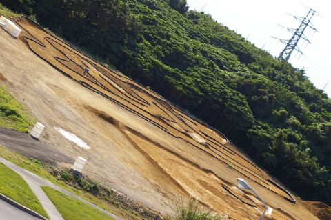 1986 Ford Bronco - A dirt RC track is laid out on a grassy and wooded hillside under a bright sky.