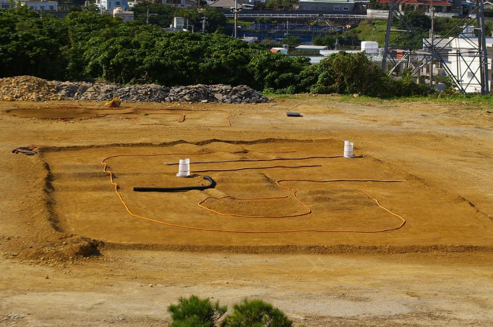 Construction site with trenches and orange hoses, two white barrels visible