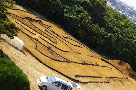 1986 Ford Bronco - A white SUV is parked near a dirt track designed for remote-controlled vehicles, surrounded by greenery.