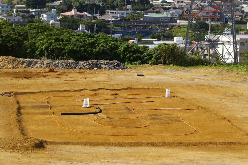 Excavation site with trenches and orange piping, residential buildings in background