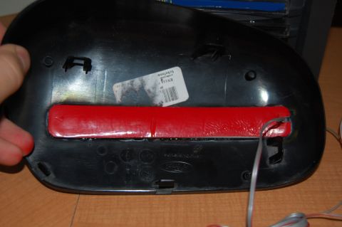 1985 Mercury Grand Marquis - The underside of a black car side mirror housing is shown, with a red strip and wiring.
