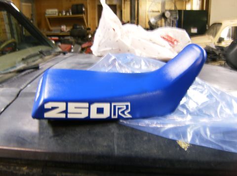 2000 Ford E350 - A blue motorcycle seat with '250R' branding is displayed on a surface in a workshop.