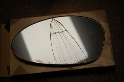 2002 BMW M3 - A cracked side mirror glass is shown resting on a cardboard box, with website text visible at the bottom.