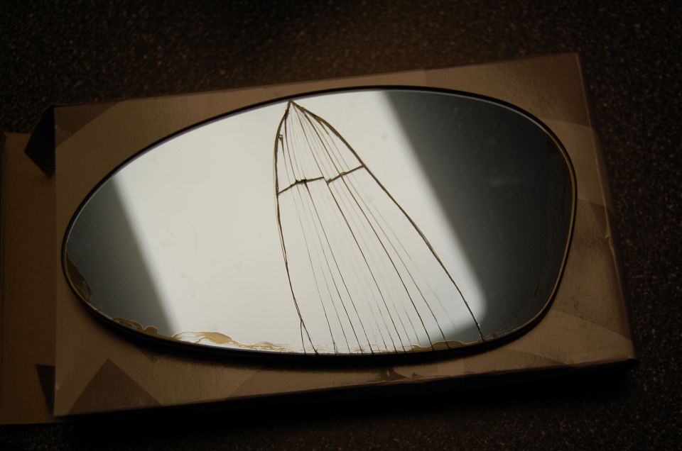 Cracked oval side mirror glass with fanned fracture lines on cardboard box
