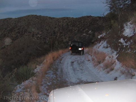 1996 Ford C-350 (Centurion Conversions) - Two vehicles navigate a snowy, mountainous dirt road at dusk.