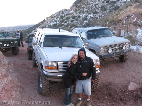 1996 Ford C-350 (Centurion Conversions) - A couple stands in front of a lifted white 1996 Ford C-350 Centurion Conversions SUV during an off-road trip.