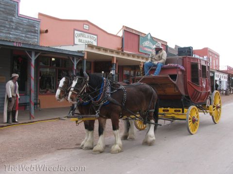 1996 Ford C-350 (Centurion Conversions) - A stagecoach pulled by two horses is parked on a dirt road in front of historic buildings, including Campbell & Hatch Billiards.