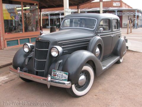 1996 Ford C-350 (Centurion Conversions) - A vintage 1935 Chrysler Airflow sedan is parked in front of a row of old-fashioned storefronts.