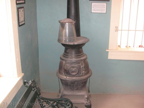 1996 Ford C-350 (Centurion Conversions) - An old-fashioned wood-burning stove is shown with a coffee pot, beside a metal bench.