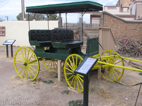 1996 Ford C-350 (Centurion Conversions) - A horse-drawn carriage with a canopy and tufted seats is displayed outdoors with signage.