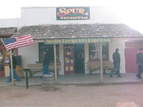 1996 Ford C-350 (Centurion Conversions) - A western-themed storefront features 'Spur Western Wear' and 'Wells Fargo & Co Express' signage, with people walking on the wooden boardwal…